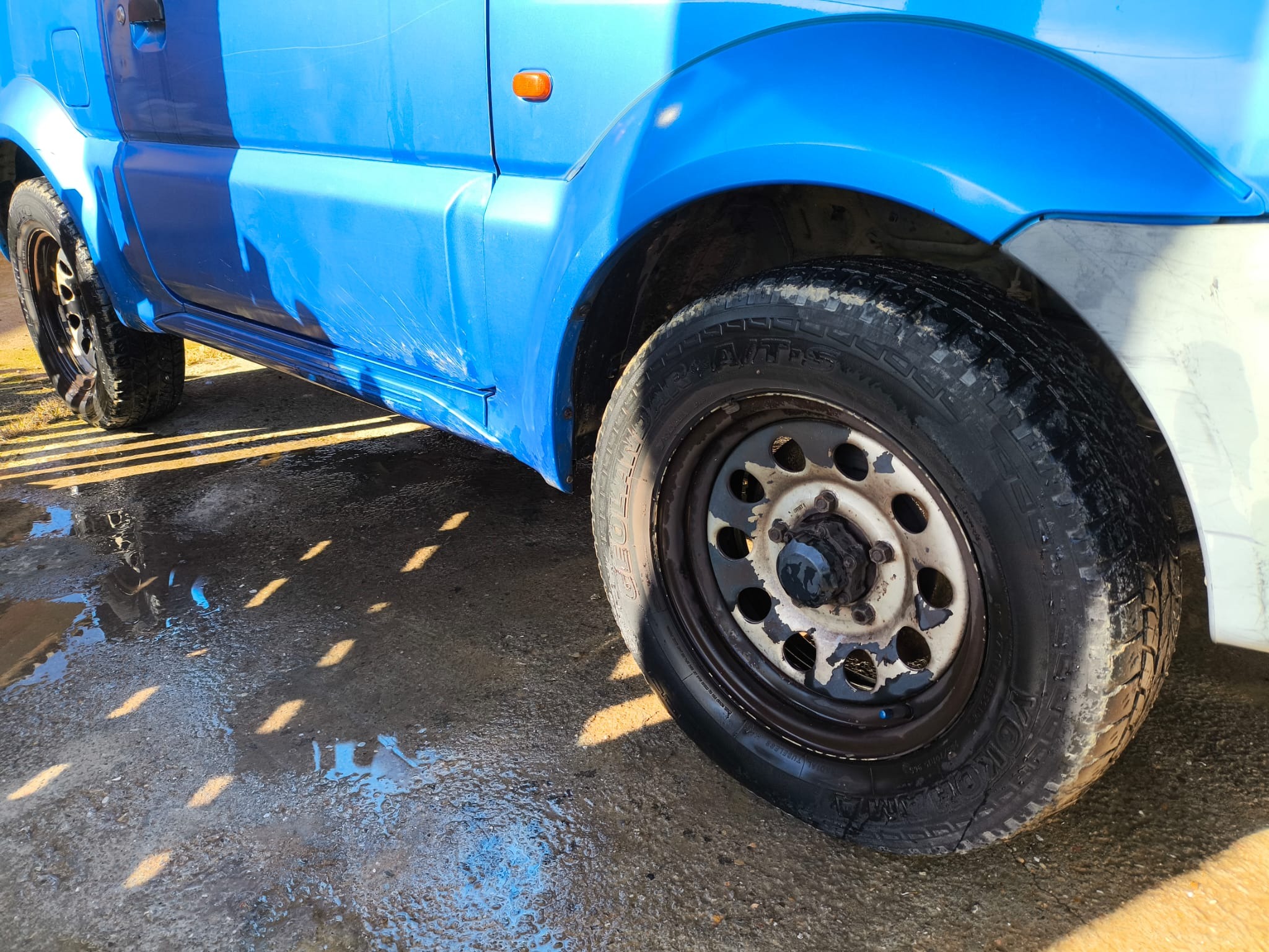 Rueda delantera izquierda: llanta metálica pintada en negro con neumático todo-terreno